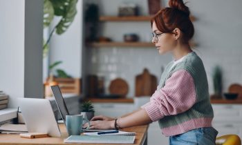 A woman working from home at a kitchen counter on a laptop.