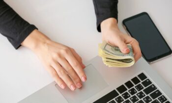 A woman holding cash while using her laptop.