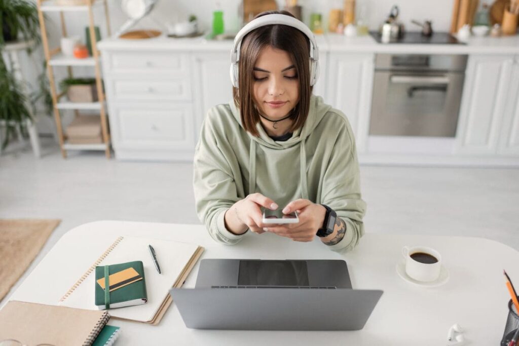 A woman working at home, sitting at her kitchen table and using her phone.