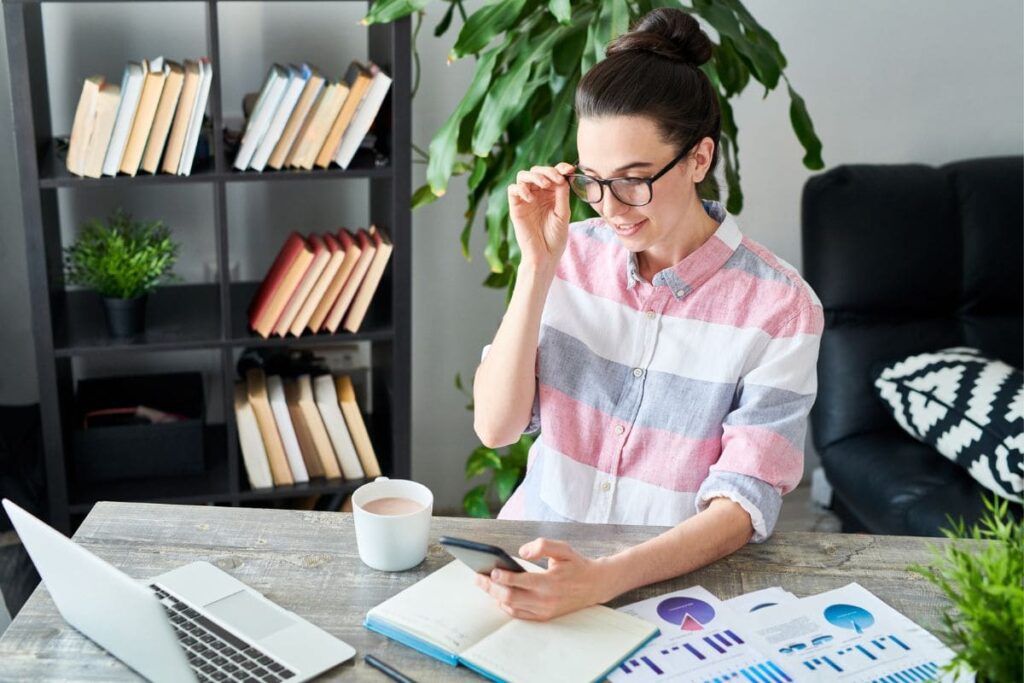 A happy woman working at home and using her phone.