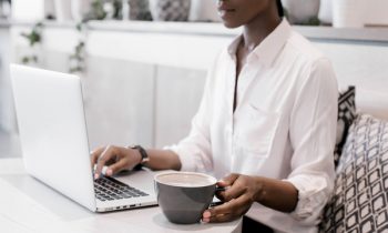 Modern woman working at her laptop drinking a cup of coffee