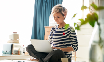 Beautiful Asian woman sitting on bed & working from home on laptop