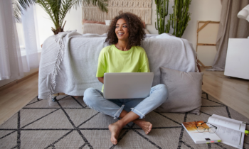 Cheerful young dark skinned woman sitting on floor using laptop and shopping online for blog post Rakuten Review