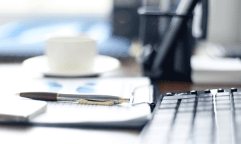 computer keyboard with notebook, pen, and coffee mug