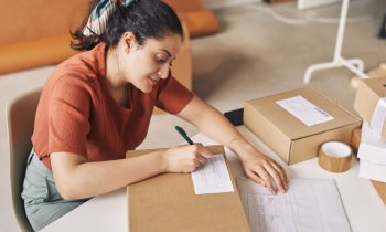 A woman online seller, writing on a shipping package label.