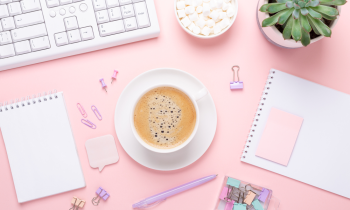 feminine office space with keyboard, plant, notebook, pens, and a latte