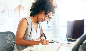 A woman working from home at a desk and writing in a notebook.