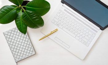 Home office desktop with laptop, ficus plant, notepad, and pen