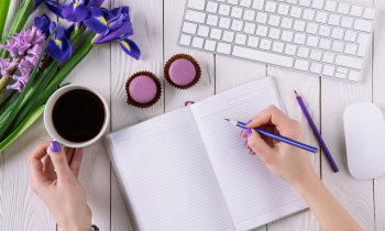 Woman with painted finger nails drinking coffee writing poetry in a notebook