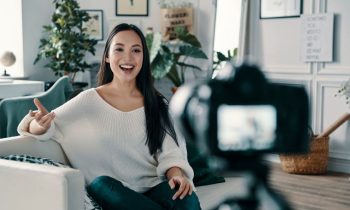 A content creator sitting in her living room, filming a video using a DSLR camera.