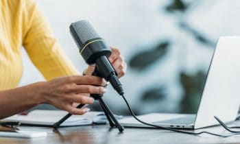 A woman working from home at a desk with a microphone and laptop.