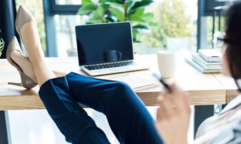 A woman working from a home office, resting her feet on her desk.