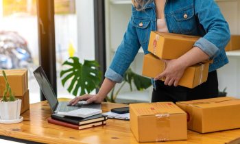 Online retail store owner checking orders on her laptop and sorting packages.