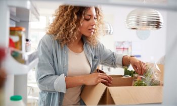 A busy mom sorting and putting away groceries from a boxed meal planning service.