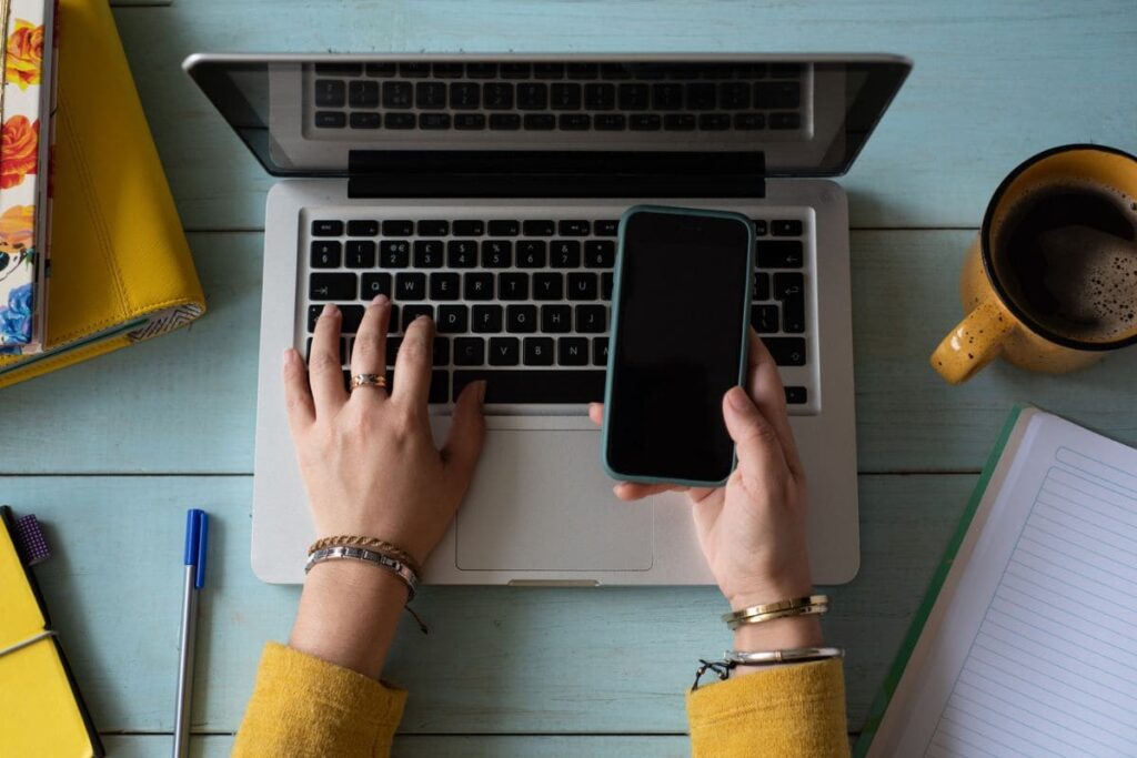 Overhead view of a woman holding a cell phone while working on her laptop.