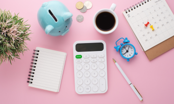 Overhead view of desk, notebook, coffee, pen, piggy bank and plant