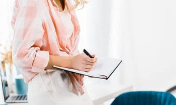 Image of woman working at home office desk and writing in a notebook