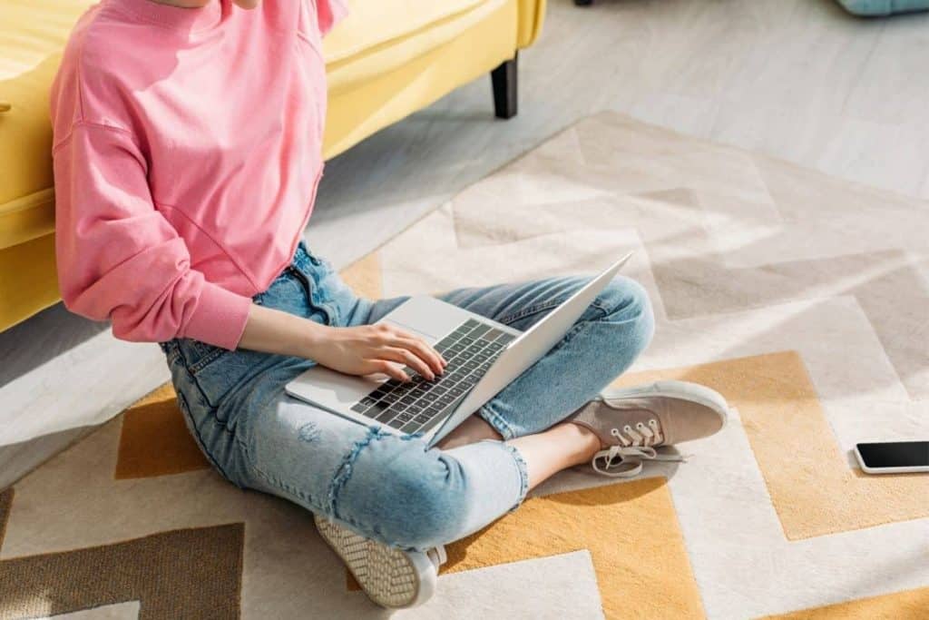 Woman sitting on the floor in her living room, working from home on a laptop for UserTesting