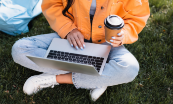 Woman in torn jeans drinking coffee taking survey with Branded Surveys on her laptop