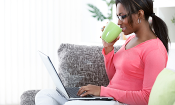 Woman sitting on a sofa drinking coffee working on her laptop