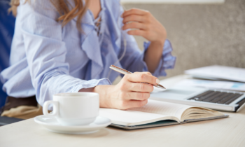 Woman writing in a note book researching how to write a cover letter on ler laptop