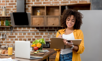 Women writing in a notebook while working from home in her kitchen