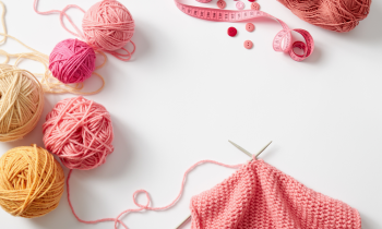 Yarn, knitting needles, buttons, and a tape measure sitting on desk