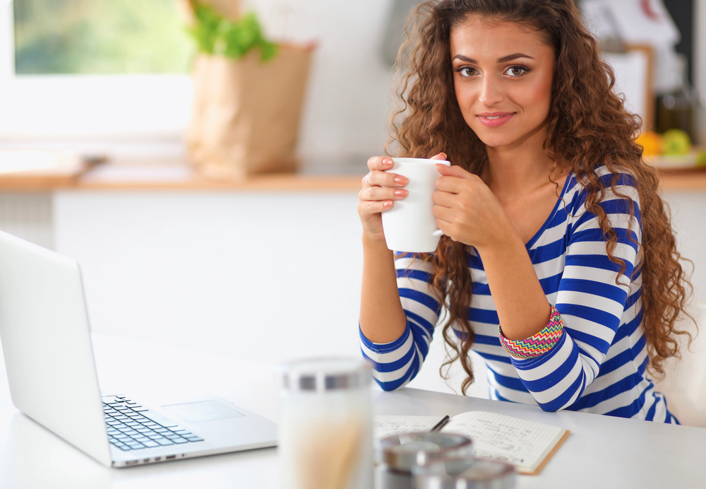 Young woman drinking coffee working on her laptop for her remote internet research job