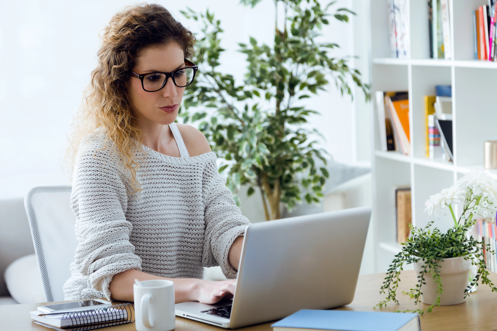 Young woman with glassed working on her laptop at home for her online editing job