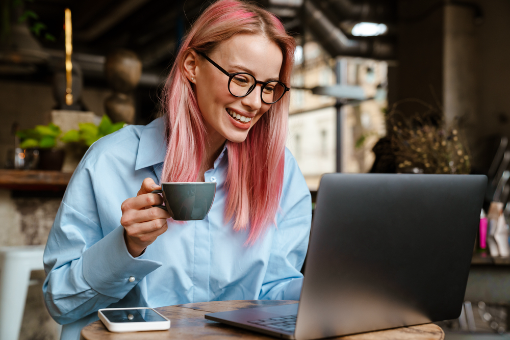 Young woman with glasses and pink hair looking at her laptop trying to get a work from home job