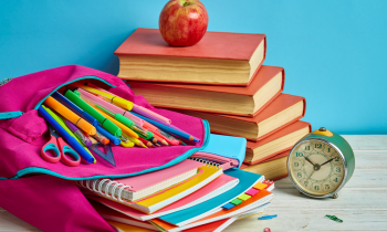 colorful back-to-school backpack stuffed with notebooks, pens, and folders, books, and a clock